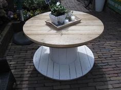 a wooden table sitting on top of a brick walkway next to flowers and potted plants