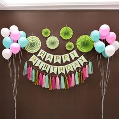 a happy birthday banner with balloons and tassels on the wall in front of it