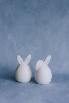 two white bunny shaped candles sitting side by side on a blue tableclothed surface