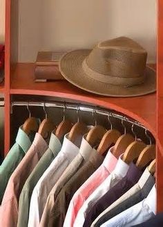 a hat is sitting on top of a shelf next to some shirts and pants in a closet