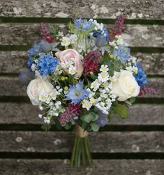 a bouquet of flowers sitting on top of a wooden bench with white and blue flowers