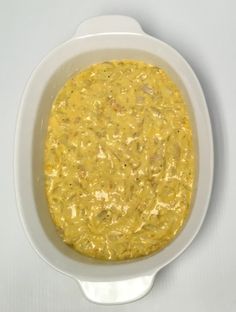 a white bowl filled with yellow soup on top of a table next to a spoon