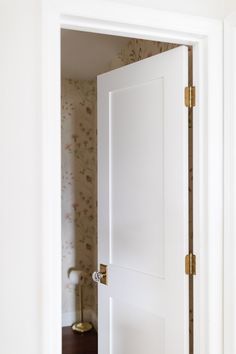 an open door in a white room with floral wallpaper