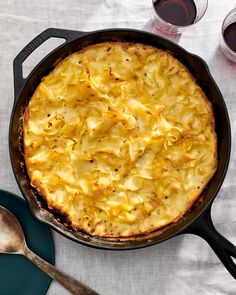 a casserole with cheese and sauce in a skillet next to two glasses of wine