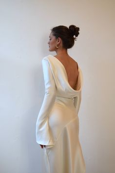 a woman in a white dress standing against a wall with her back to the camera