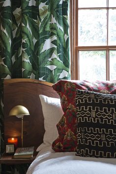 a bed with two pillows on top of it next to a night stand and window