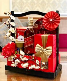 a red gift box filled with liquor and flowers sits on a table next to a fan