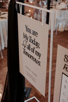 a sign hanging from the side of a pole in front of tables with white linens