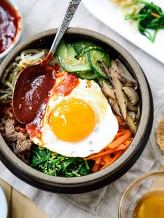 a bowl filled with meat, vegetables and an egg sitting on top of a table