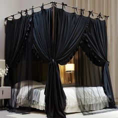 a black canopy bed with sheer drapes on the top and bottom, in a bedroom