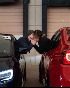 a woman leaning on the hood of a red car in front of two other cars