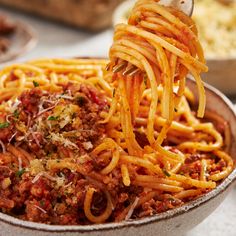 a spoon full of spaghetti being lifted from a bowl with meat sauce and parmesan cheese