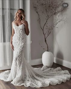 a woman standing in front of a window wearing a wedding dress with flowers on it