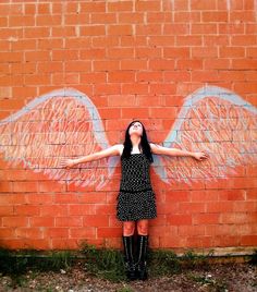 a woman standing in front of a brick wall with wings painted on it