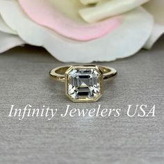 an image of a ring with a stone in the middle and flowers behind it on a table