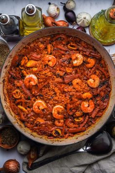 a large pan filled with food on top of a table next to spices and utensils