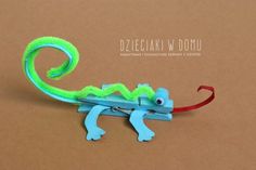 a green and blue toy lizard sitting on top of a piece of cardboard with red string