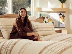 a woman sitting on top of a bed next to pillows