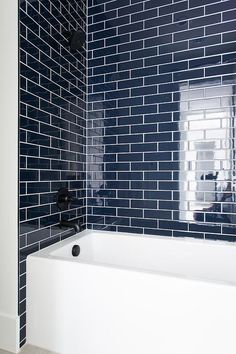 a bath tub sitting under a window next to a tiled wall in a white bathroom