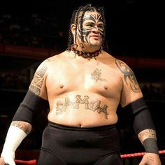 a man with tattoos on his face standing in front of a roped off ring