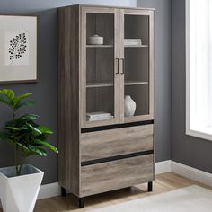 a wooden cabinet sitting next to a potted plant in a room with gray walls