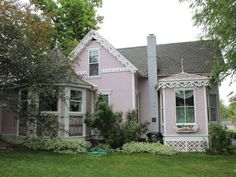 a pink house with white trim on the front and side windows is surrounded by greenery