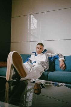 a man sitting on top of a blue couch next to a glass table with a shoe