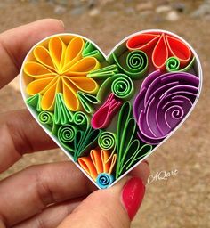 a hand holding a heart shaped ornament with colorful flowers on it's side