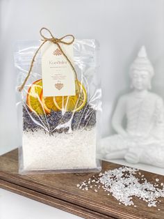 a bag of sea salt and an orange on a wooden table next to a buddha statue