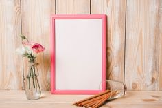 an empty pink frame next to some cinnamon sticks and a vase with flowers on a wooden table