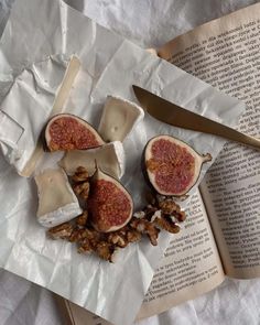 an open book with figs and nuts on it next to a knife, fork and spoon