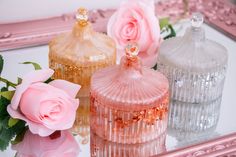 three pink roses sitting on top of a table next to two glass bottles and a mirror