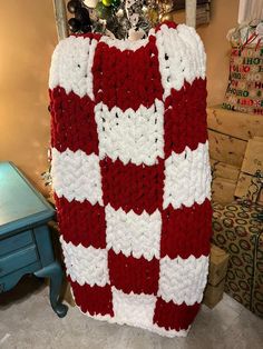 a red and white crocheted blanket sitting on top of a table next to a christmas tree