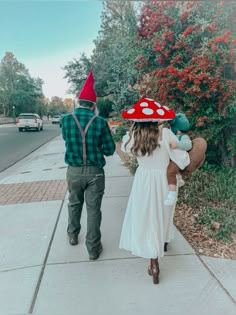 a man and woman are walking down the sidewalk with gnome hats on their heads while holding hands