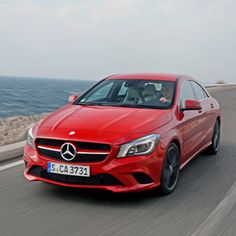 a red mercedes cla driving down the road