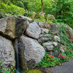 there is a rock wall with a waterfall coming out of it and flowers growing on the rocks