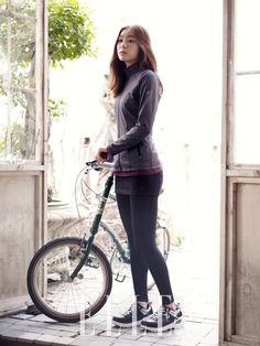 a woman standing next to a bike in front of a window