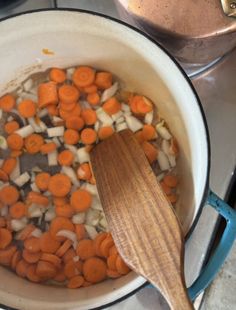 carrots and onions are being cooked in a pot on the stove with a wooden spoon