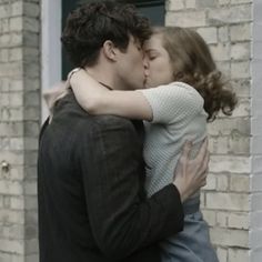 a man and woman kissing in front of a brick building