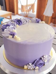 a purple cake with white frosting and flowers on top is sitting on a table