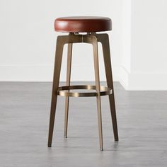 a stool with a brown leather seat and metal frame on the bottom, in front of a white wall