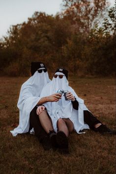 two people dressed in black and white sitting on the ground with one holding a can