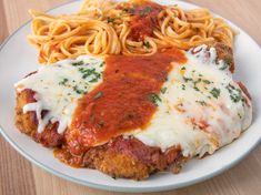 a white plate topped with pasta and meat covered in sauce on top of a wooden table