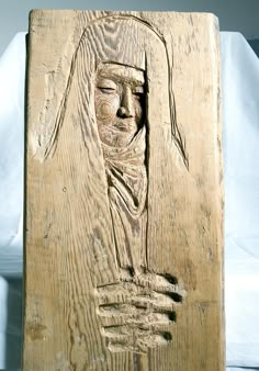 a carved wooden plaque with a man's head and hands in the center, on a white surface