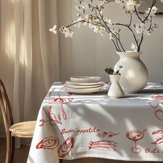 a white vase filled with flowers sitting on top of a table next to plates and cups