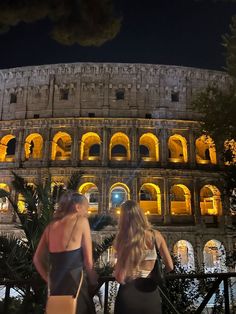 two women standing in front of the colossion at night, with their backs turned to the camera