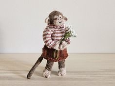 a stuffed monkey holding a bouquet of flowers on top of a wooden table in front of a white wall