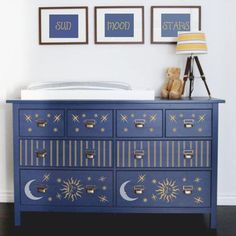 a blue dresser with gold stars and moon decals on it, next to a teddy bear