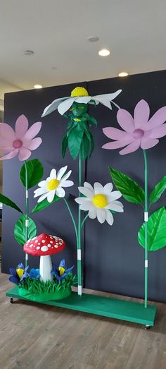 paper flowers and mushrooms on display in front of a large wall with a mushroom at the center