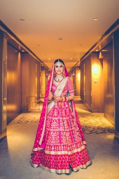 a woman in a red and pink bridal gown standing on a hallway with her hands behind her back